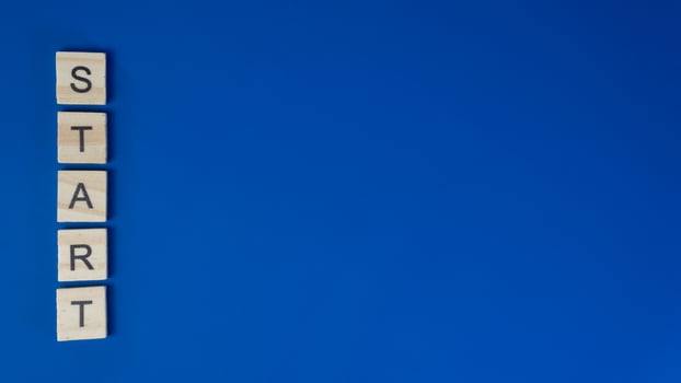 Vertical Word START with Wooden Letter Tiles on Solid Blue Background photo