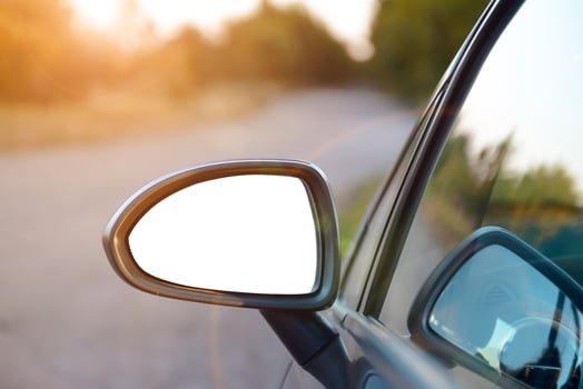 A car side view mirror is seen in the road photo
