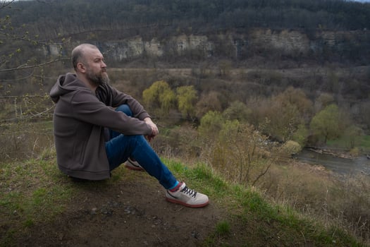 Man sits quietly by a riverbank overlooking a serene landscape in early spring photo