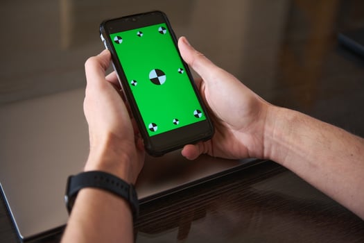 Person Holding Smartphone With Green Screen Over Laptop photo