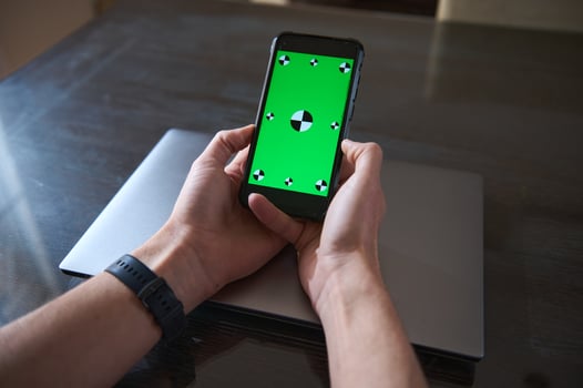 Person Holding Smartphone With Green Screen Over Laptop on Wooden Desk photo