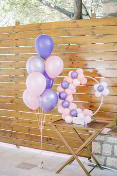 Round decor of colorful inflatable balloons stands on a table near a wooden fence photo