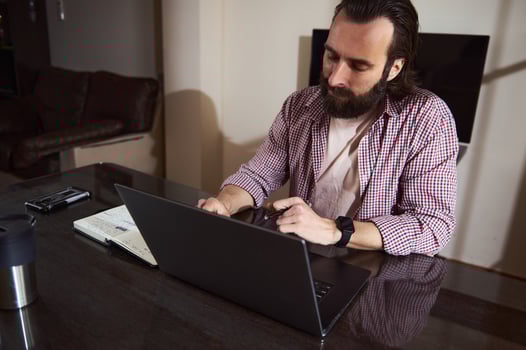 Focused Man Working on Laptop While Taking Notes in a Home Office photo