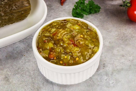 A bowl of green salsa next to a bowl of tomatoes photo