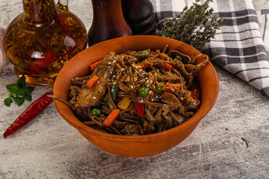 A bowl of noodles with vegetables and a bottle of olive oil photo