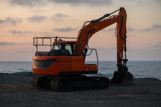 Excavator poised for work at the shoreline during a tranquil sunset over the ocean photo