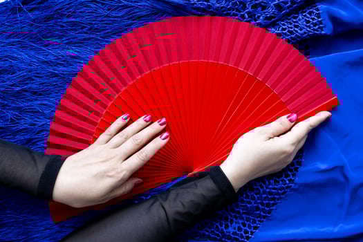 Close up of red hand fan with caucasian female hands holding it on blue fabric photo