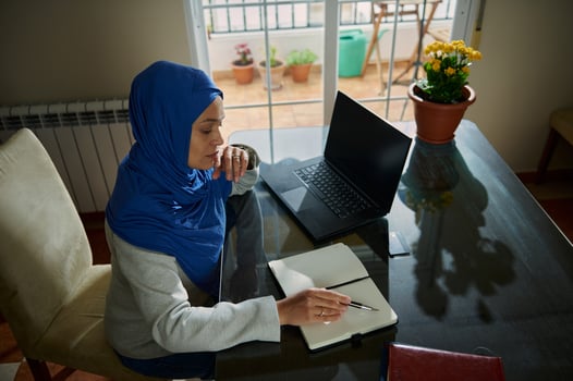 Muslim Woman Working Remotely with Laptop and Notes in a Cozy Home Office photo