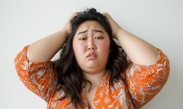 Woman expressing frustration with hands on head, showcasing emotions and stress in a bright orange outfit, mental health awareness concept photo