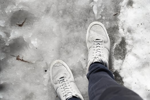 Legs in sneakers standing in the melting snow on the sidewalk. First-person view. Spring thaw concept photo