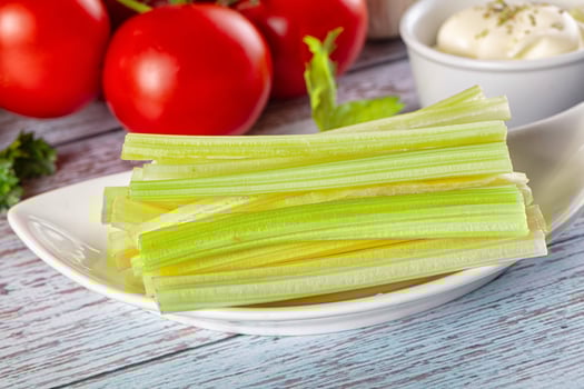 Celery sticks on a white plate with tomatoes and herbs photo