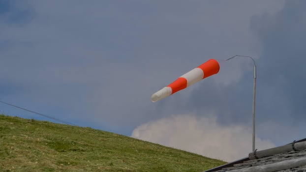 Wind direction indicator waves gracefully above a lush green hillside under a clouded sky in a serene rural setting photo
