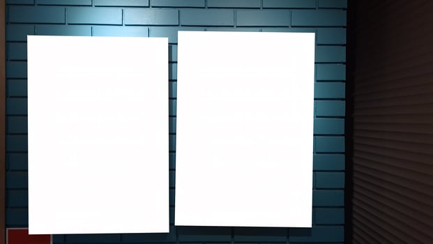 Two blank vertical posters on blue brick wall in dimly lit interior photo