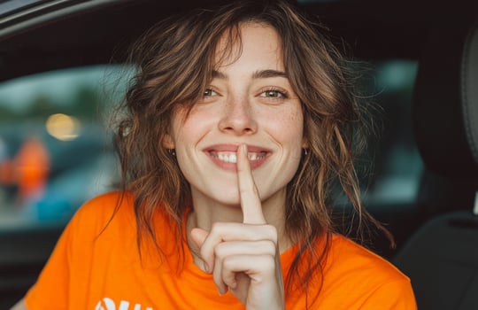 A woman in an orange shirt is holding her finger to her lips photo