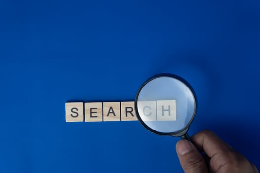 Hand Holding Magnifying Glass Over Wooden Letters Spelling Search on Blue Background photo