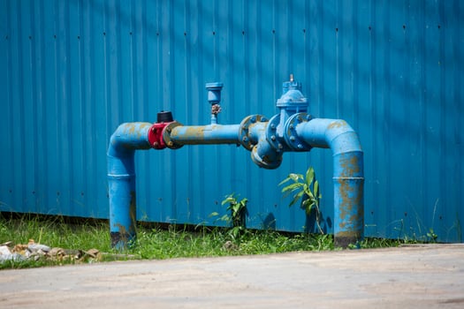 blue industrial water pipe system with visible rust near a corrugated metal wall in an outdoor setting photo
