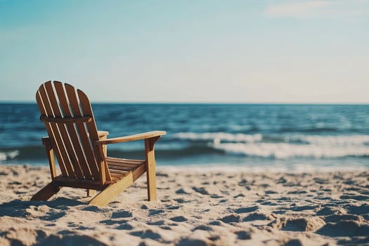 A wooden chair sits on the beach near the ocean photo