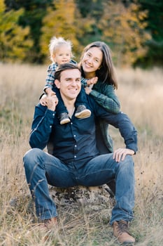 Smiling mom hugging dad from behind with a little girl on his shoulders in a clearing photo
