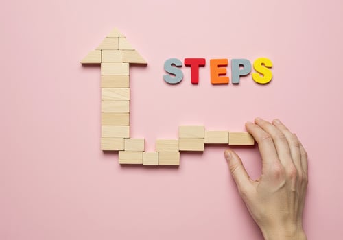 Hand holding wooden blocks with the word steps on pink background. photo