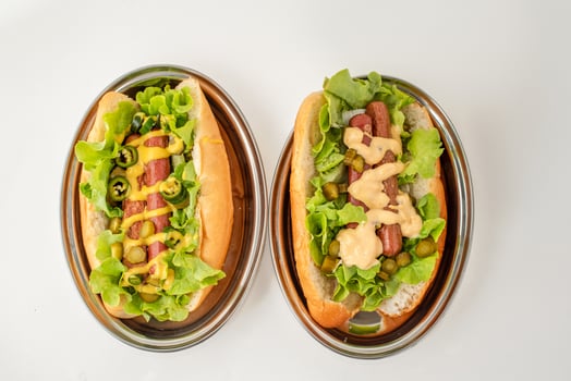 Flat lay of two hot dogs on oval stainless steel plates, garnished with lettuce, pickles, mustard, jalapenos, and creamy dressing, on white background photo