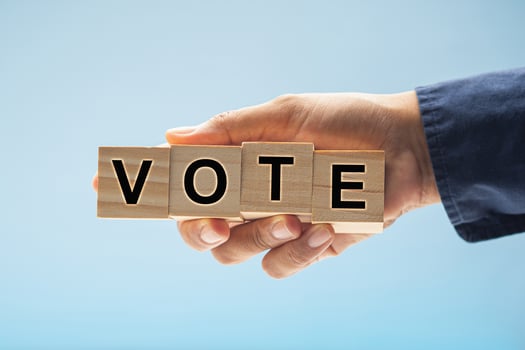 Hand holding wooden cubes with letters VOTE against a blue background photo