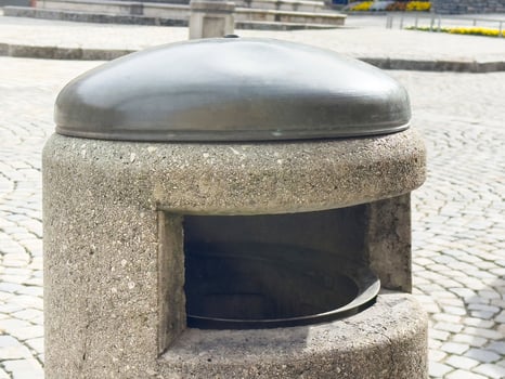 Urban stone trash bin with metal lid on cobblestone street photo