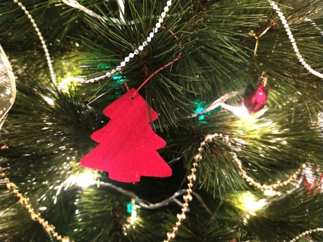 Close-up of a Christmas tree adorned with twinkling lights, red ornament, and elegant gold and pearl garlands. A charming red felt tree-shaped decoration adds a festive touch. photo