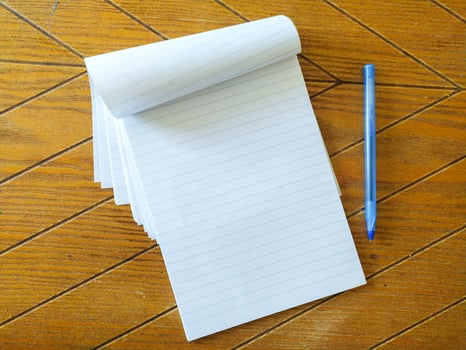 Blank lined notepad and blue pen on a wood table. Perfect for education, business, or office concepts. Clean, simple, and ready for your message. Ideal for mockups or website backgrounds. photo