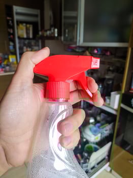 Hand holding spray bottle, red nozzle, transparent liquid. Cleaning concept, home maintenance, hygiene. Illustrates protection, sanitation, routine. photo