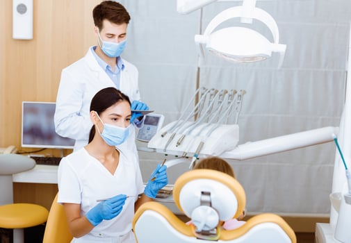 Work of specialist doctors with children teeth. Young man and woman dentists in white coats, protective masks and gloves work with medical equipment with girl in armchair in interior of modern office photo