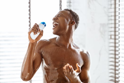 Naked African American Man Singing Holding Male Shampoo Bottle Relaxing And Having Fun Taking Shower Standing Under Water In Bathroom At Home. Men's Hygiene And Beauty Routine Concept photo