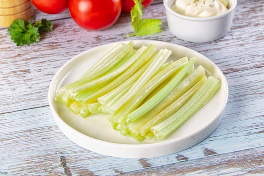 Celery sticks on a white plate with a bowl of tomato sauce and a green leaf photo
