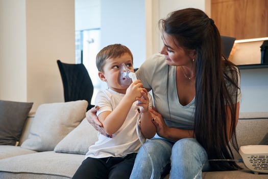 Inhalation for reducing the coughing. Mother with her little son is at home in domestic room photo