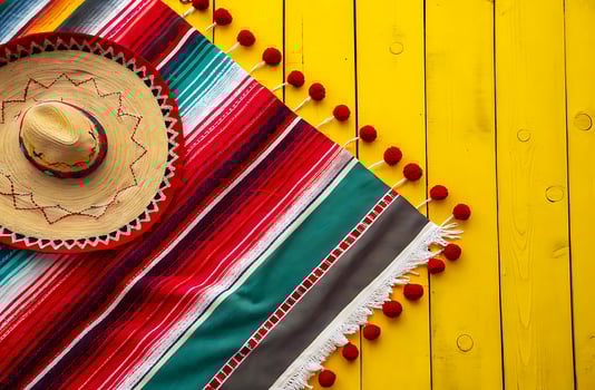 Vibrant Mexican Serape Blanket with Red Pom-Pom Trim on Bright Yellow Wooden Background for Cinco photo