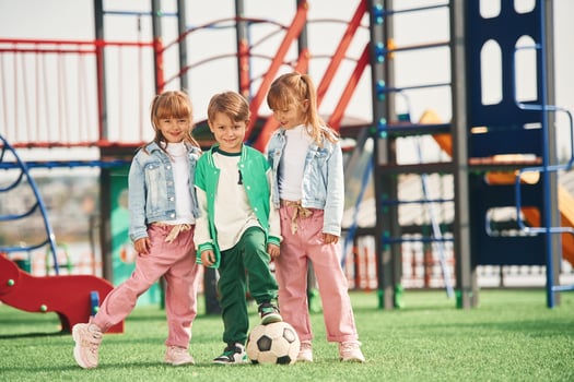 Boy is in, green ,clothes, with soccer ball. Kids are having fun on the playground photo