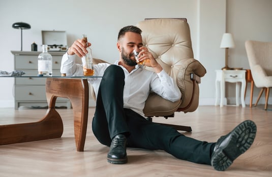 Sitting on the floor, sad. Upset young man drinker alcoholic is indoors photo