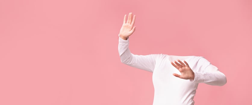 A headless figure in a white long-sleeve shirt poses against a soft pink background, emitting a playful vibe. The composition focuses on body language and movement, evoking a sense of whimsy. photo