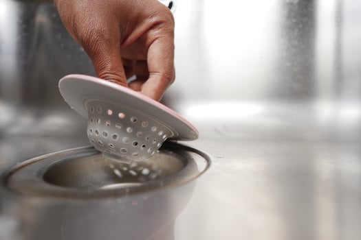 Hand lifting a kitchen sink strainer to clean it in a home kitchen photo