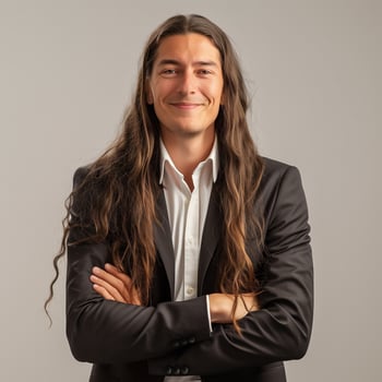Smiling businessman with long, wavy brown hair wearing a black suit and white shirt, standing confidently with crossed arms photo