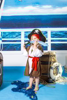 A young child dressed as a pirate stands in front of a blue background with a pi photo