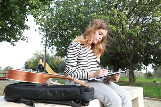 Girl Writes Notes On A Sheet Music To Play Them With Ukulele Outdoor photo