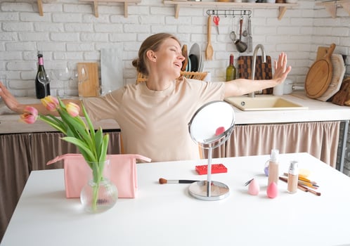 happy woman applying makeup sitting in the kitchen in the morning photo