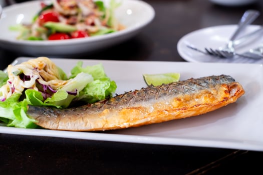 Grilled mackerel served on a white plate with fresh green salad, topped with creamy dressing and a slice of lime. A healthy and delicious seafood dish perfect for food content photo