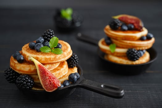 Golden pancakes, adorned with vibrant berries, contrast beautifully against a black wooden background photo