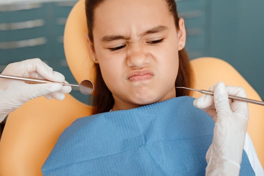 Natural children emotions and toothache treatment. Little hispanic girl in medical chair looks with disbelief at instruments in hands of doctor in rubber gloves in dental clinic, pov, close up photo