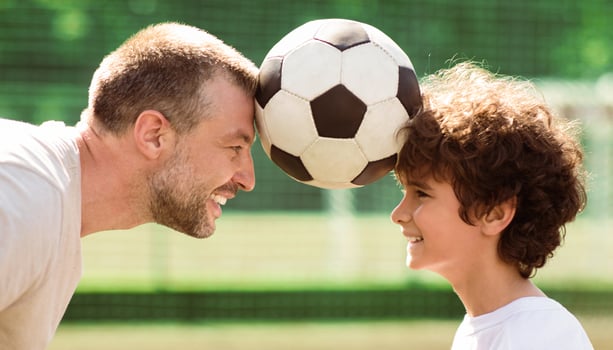 Competition Concept. Closeup of adult man and small boy holding soccer ball between forehead photo