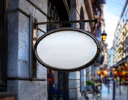 An oval shaped white blank store sign hanging outside a shop in city photo