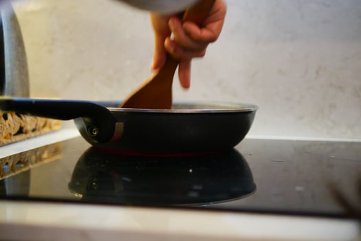 Cooking on a stovetop with wooden spoon and frying pan in kitchen photo