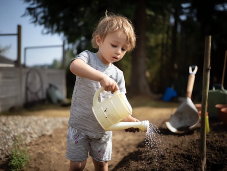 Toddler watering plants in garden. Happy child. photo