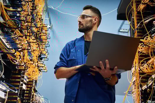 Holding, laptop. Young man is working ,with internet equipment and wires in server room photo